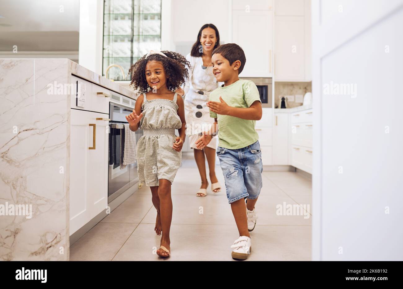 Mutter, Kinder spielen zusammen Laufspiel und Familie Bonding in der Küche zu Hause. Lächelnde verspielte Mutter, glücklich aufgeregt energische Kinder und aktiv Stockfoto