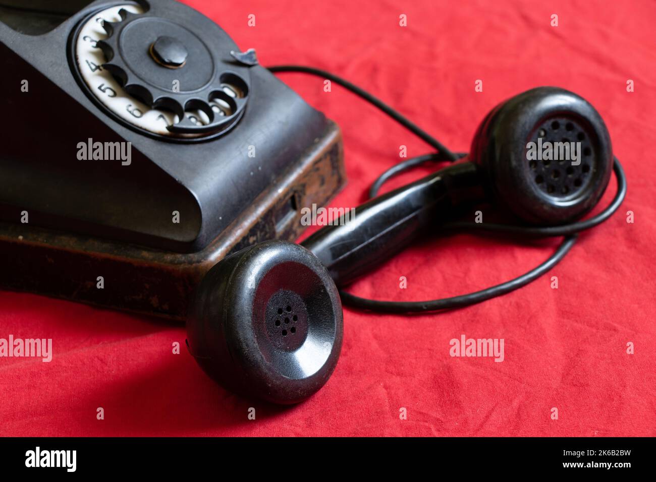 Ein altes schwarzes Telefon steht auf einem roten Tuch, einem alten Telefon der Vergangenheit Stockfoto
