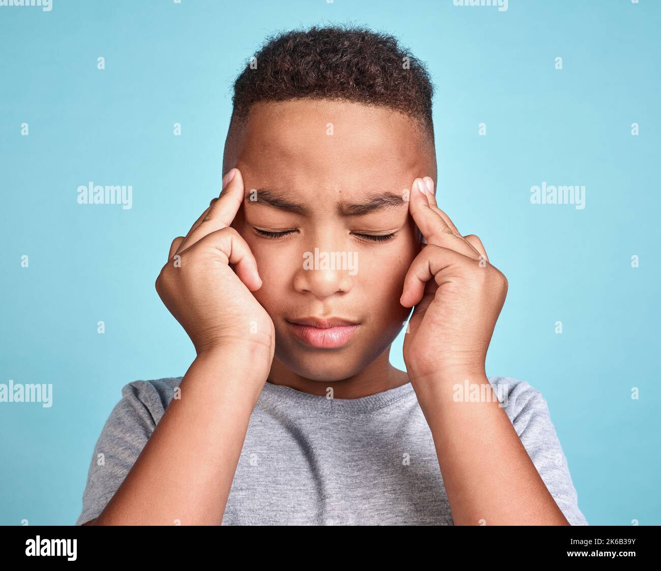 Kind mit Kopfschmerzen, Stress und psychischen Problemen oder Ermüdungsschmerzen auf blauem Studiohintergrund. Frustriert afroamerikanischen Kind, deprimiert Junge und Stockfoto