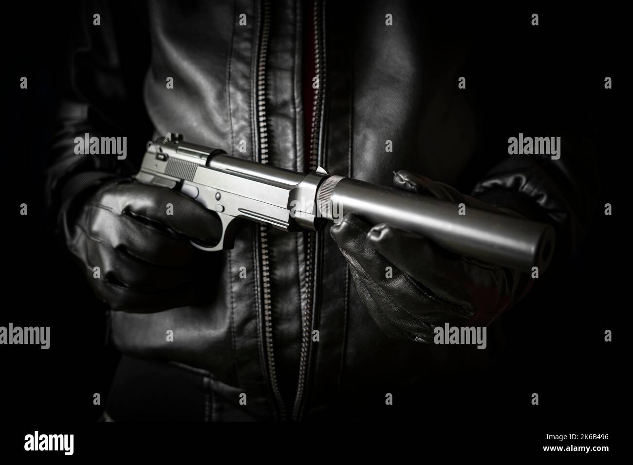 Das Konzept des Verbrechens der Banditen. Ein gefährlicher Schütze und eine schwarze Pistole auf dunklem Hintergrund. Der angeheuerte Mörder bereitet sich auf die Schießerei vor. Killer-Scre Stockfoto