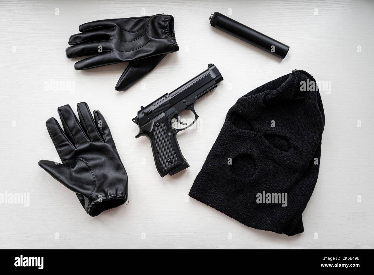Handschuhe, eine Pistole und eine schwarze Maske auf einem weißen Tisch. Beweise bei der Suche nach einem Räuber oder Mörder. Beweise für ein Verbrechen. Stockfoto