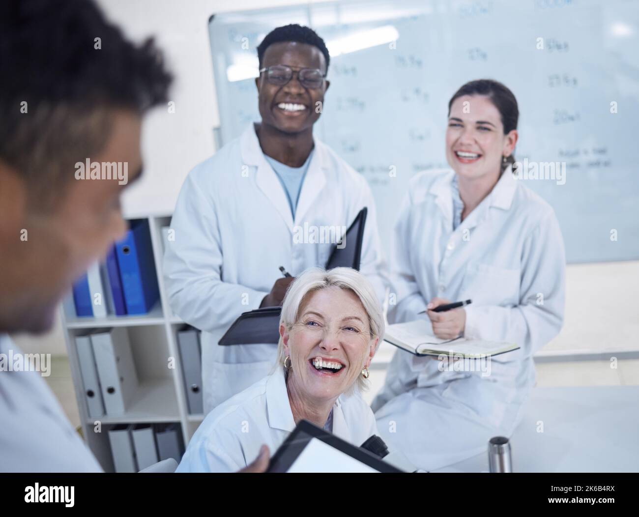 Ein vielfältiges Team junger Ärzte, die in Laborkittel lachen und über die Arbeit im Labor diskutieren Stockfoto