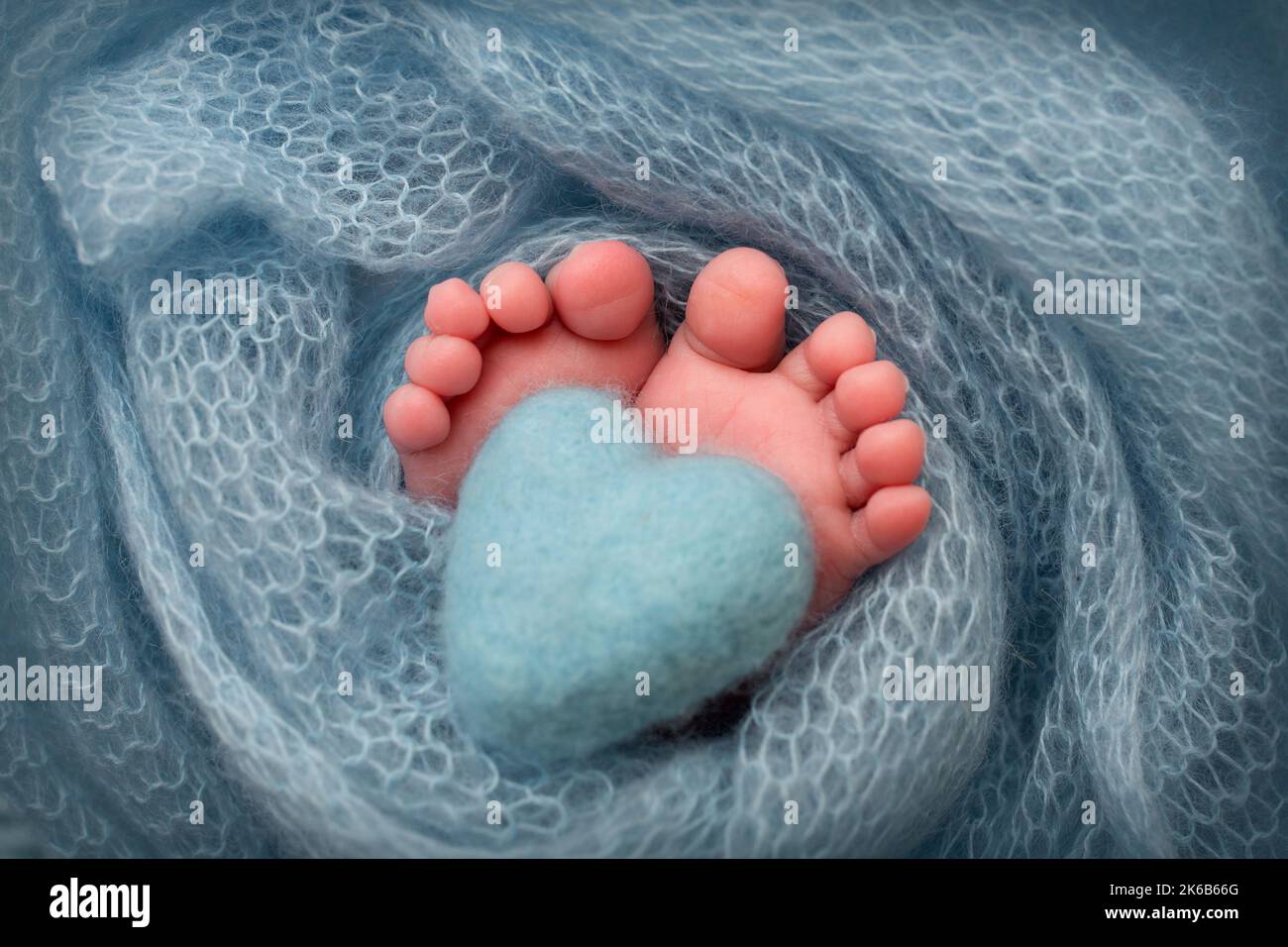 Weiche Füße eines Neugeborenen in einer türkisfarbenen Wolldecke. Gestricktes türkisfarbenes Herz in die Beine eines Babys. Makrofotografie. Stockfoto