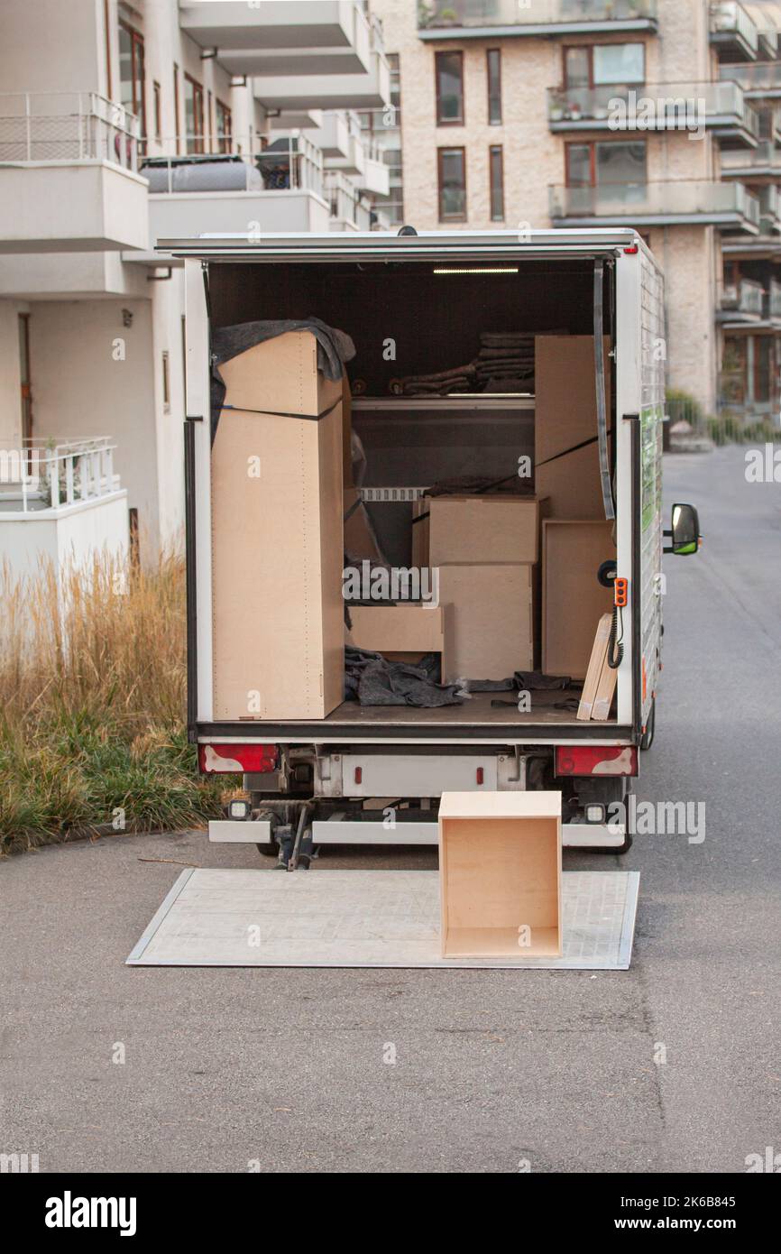 Nicht identifizierter geschlossener Transporter mit geöffneter Heckklappe vor modernen Gebäuden. Möbel und Kisten werden in den LKW geladen. Stockfoto