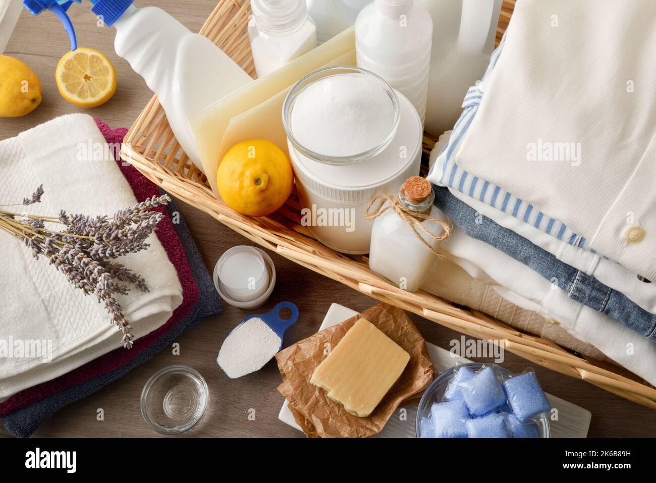 Gruppe von chemischen und alternativen Wäschereiprodukten auf einem Tisch mit gewaschenen Kleidungsstücken und Fensterhintergrund. Draufsicht. Horizontale Zusammensetzung. Stockfoto