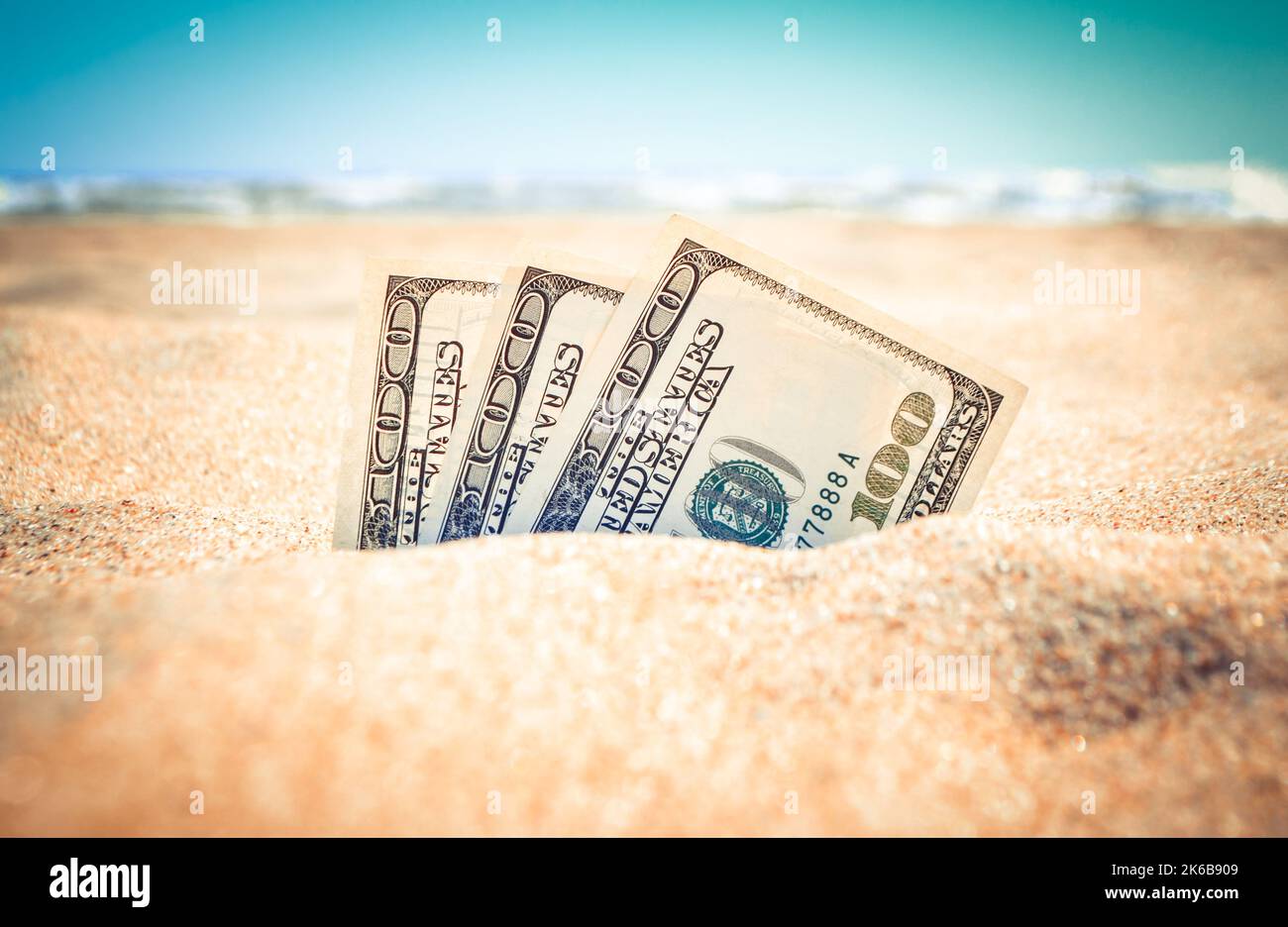 Die mit Sand bedeckten Gelddolare liegen am Sandstrand in der Nähe der Meereswellen am sonnigen Sommertag aus nächster Nähe. Geld wächst aus dem Boden. Konzept Finanzierung Geld Urlaub Relax Urlaub. Stockfoto