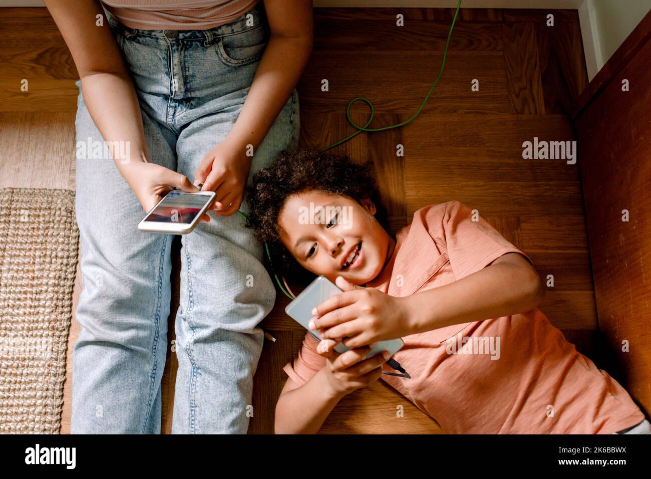 Lächelnder Junge, der zu Hause Smartphone mit seiner Schwester benutzt, während er sich auf dem Boden niederlegt Stockfoto