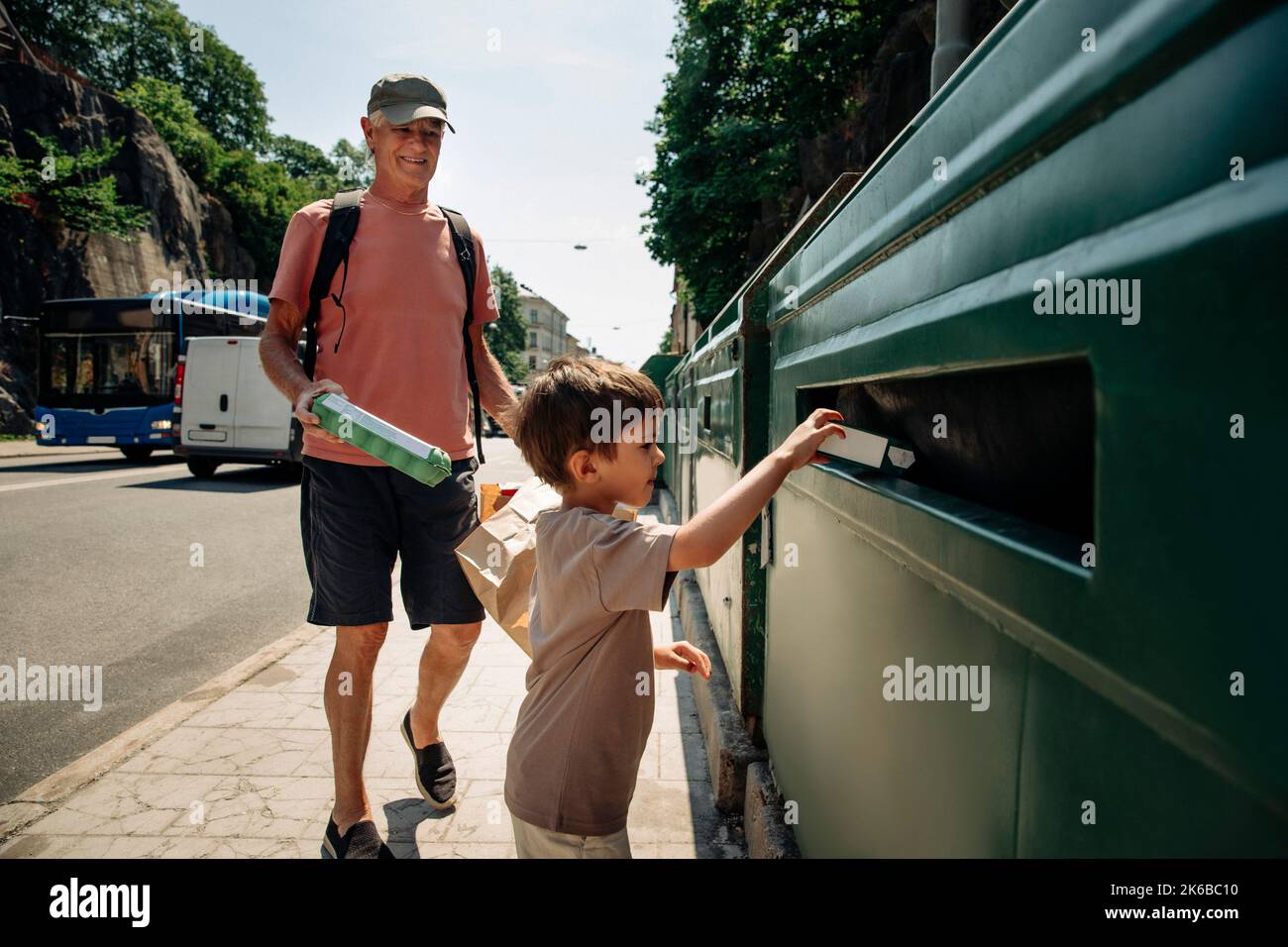 Junge, der mit dem Großvater auf dem Bürgersteig den Müll in den Papierkorb schleert Stockfoto