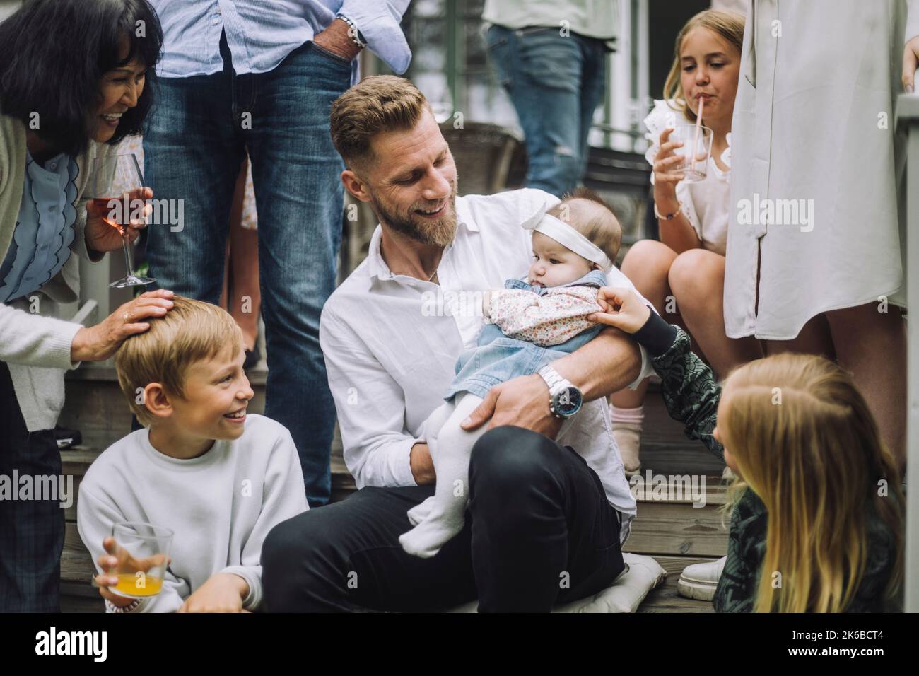 Familie spielt mit Kleinkind Mädchen gehalten von Mann auf Treppen sitzen Stockfoto