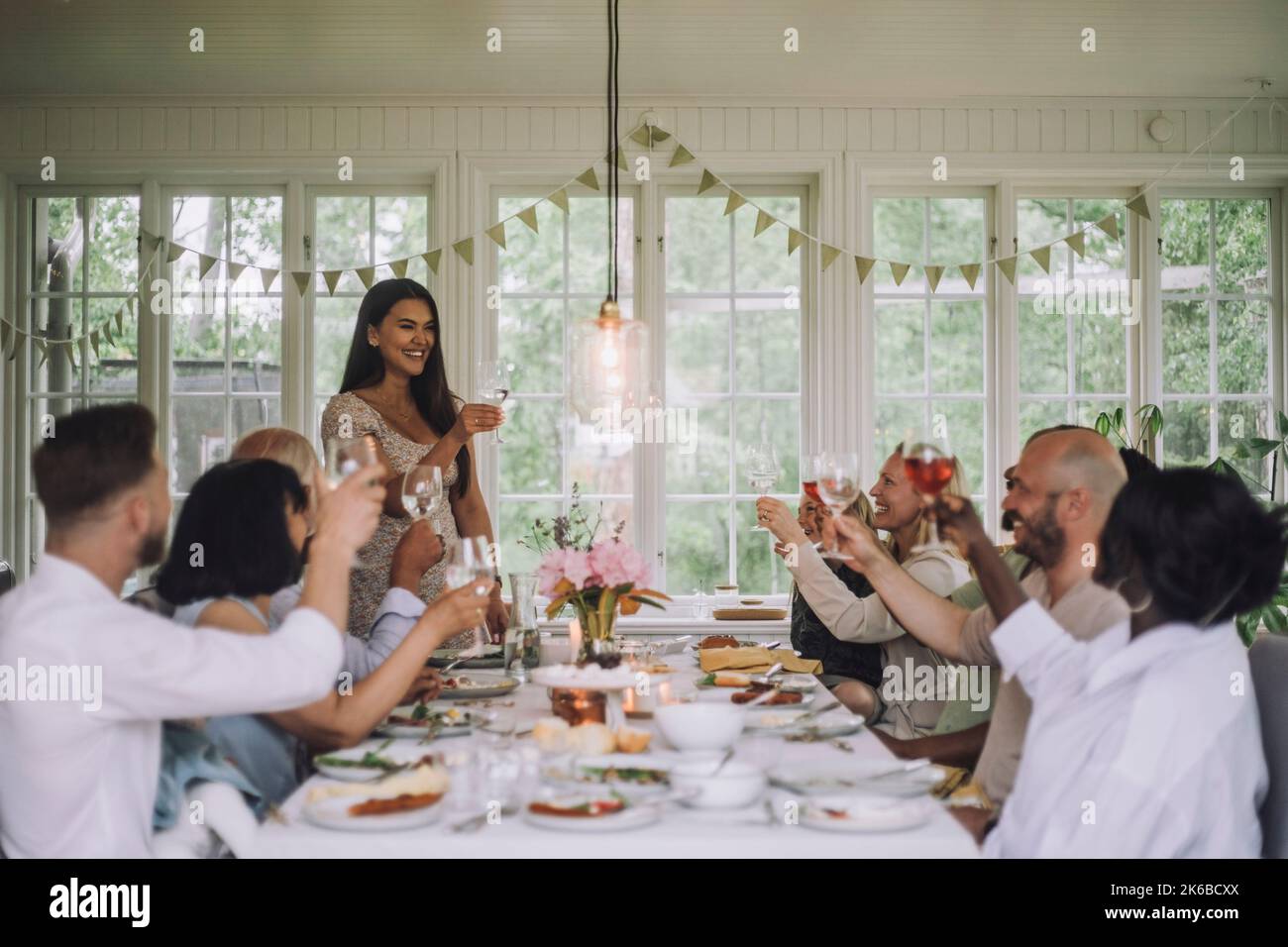 Lächelnde Frau, die während der Dinner-Party zu Hause einen Drink mit den Familienmitgliedern toasting Stockfoto