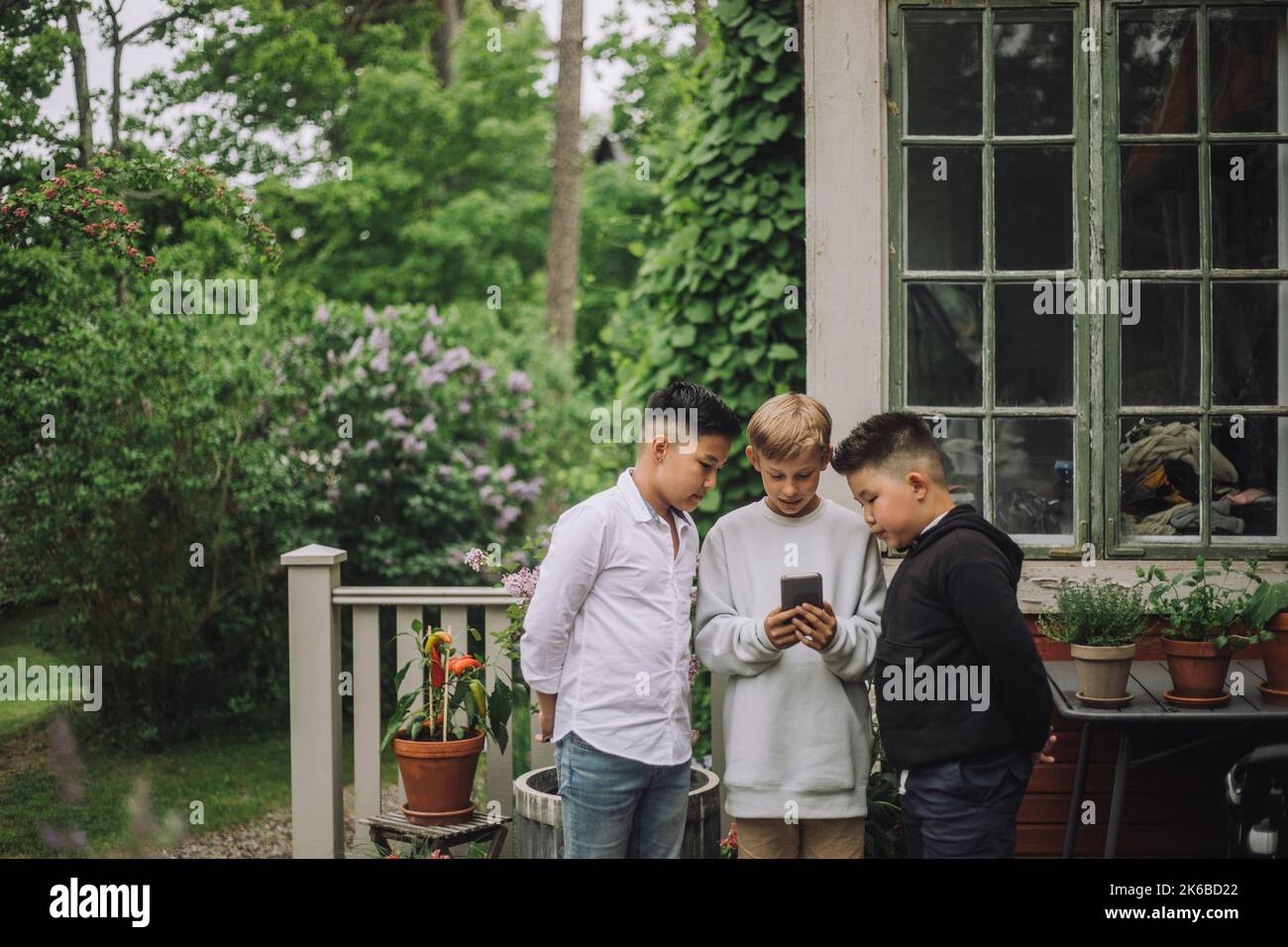 Jungen, die in der Nähe des Hauses stehen und ihr Smartphone teilen Stockfoto