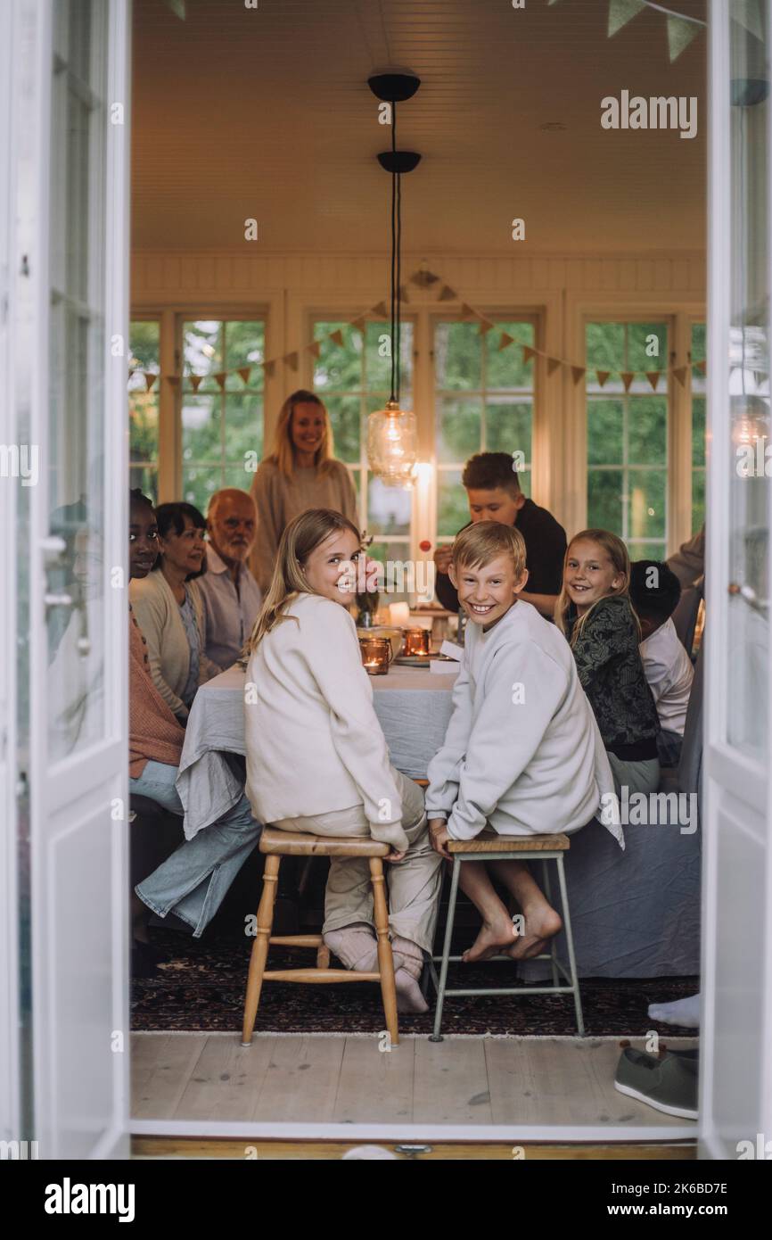 Junge und Mädchen schauten über die Schulter, während sie mit der Familie auf dem Hocker am Esstisch saßen Stockfoto