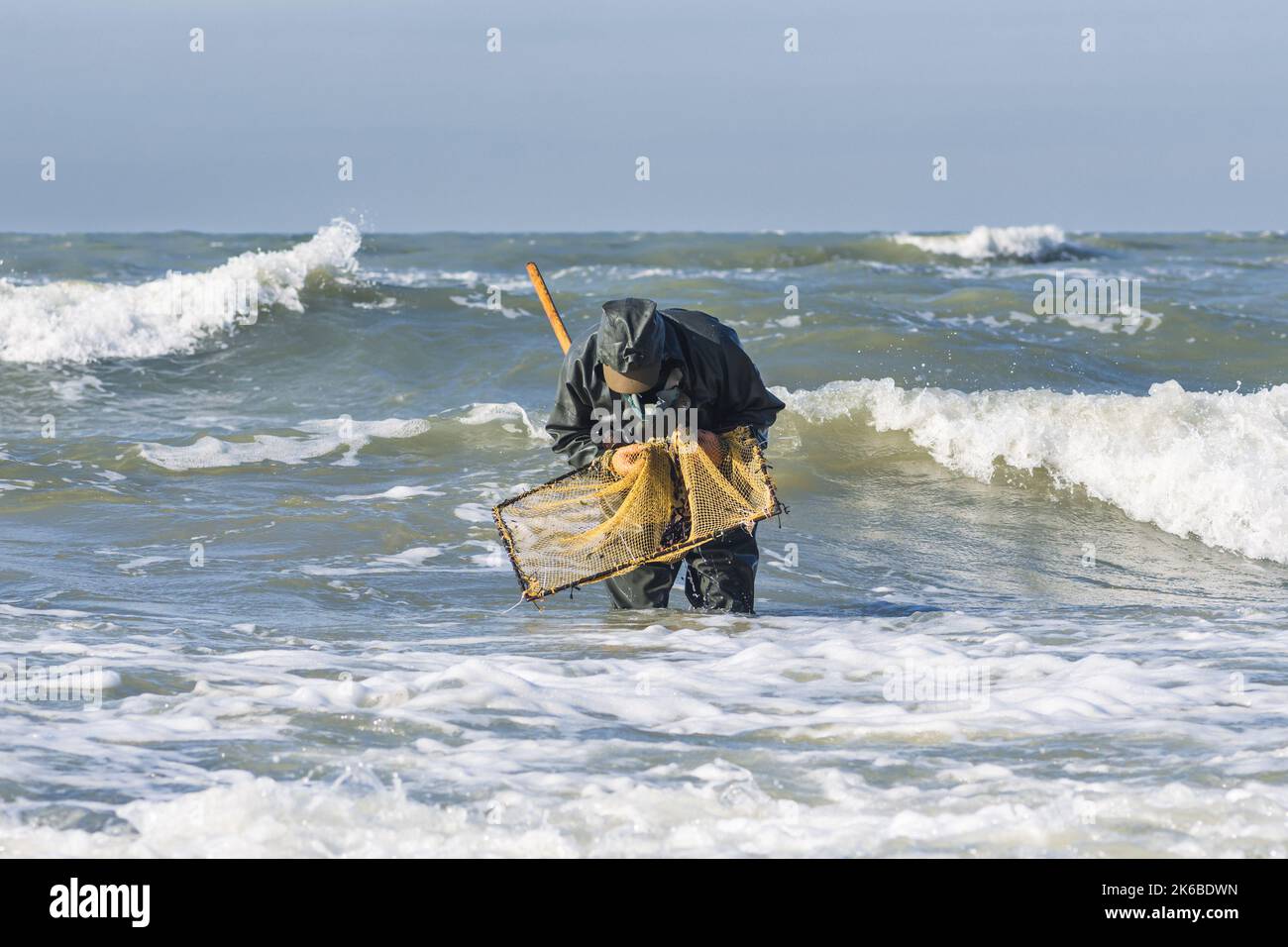 Bernsteinfang in der Ostsee. Bernsteinfnger oder Fischer mit Fischerkittel  und Stiefeln ins Meer unter groen Wellen mit Aushhlern, Fischernetz  Stockfotografie - Alamy