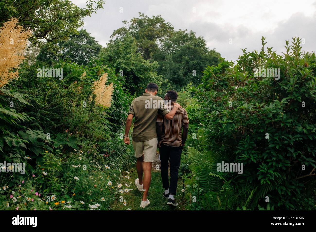 Rückansicht von männlichen Freunden, die im Garten spazieren und reden Stockfoto