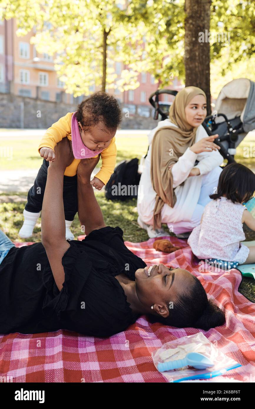 Frau spielt mit Tochter, während sie sich auf einer Picknickdecke im Park hinlegt Stockfoto