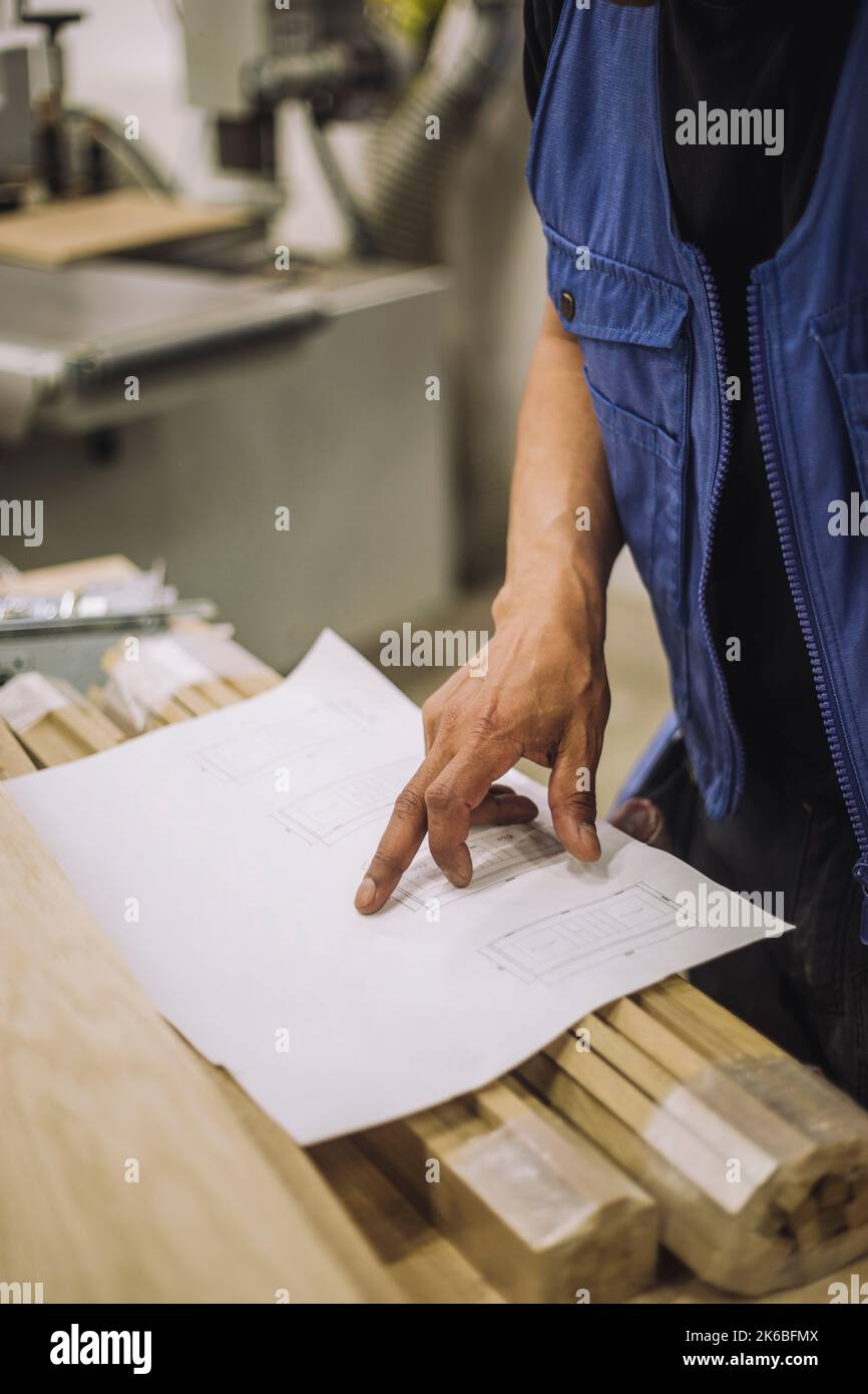 Mittelteil eines reifen Angestellten, der die Blaupause im Lagerhaus liest Stockfoto