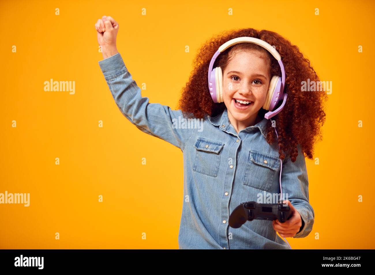 Studio Portrait Of Girl With Headphones Playing Computer Game Against Yellow Background Stockfoto