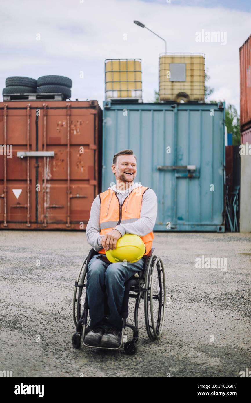 Die ganze Länge der glücklichen Bauarbeiter sitzt im Rollstuhl auf der Baustelle Stockfoto