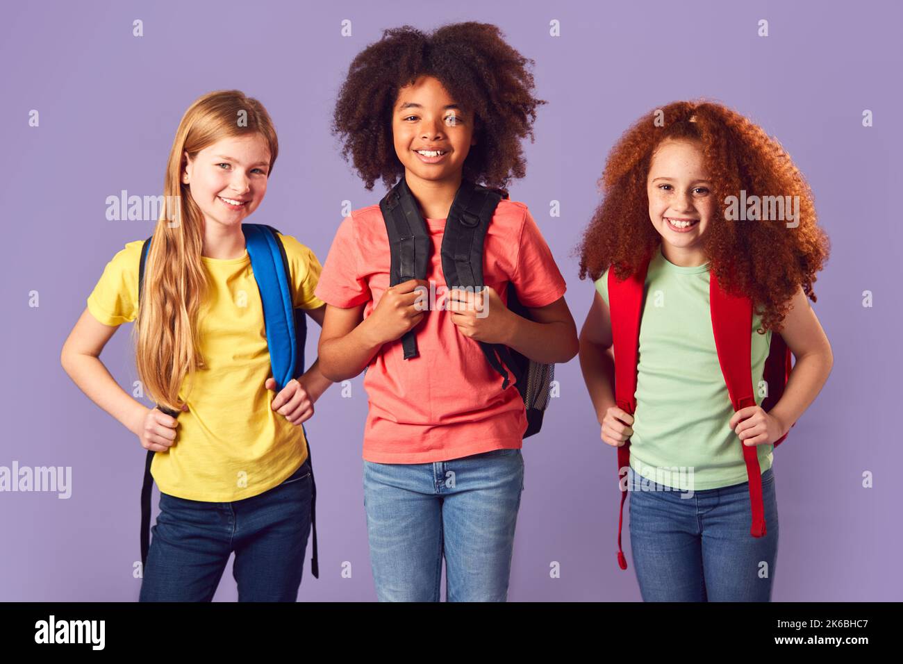Studioaufnahme Von Drei Kindern Mit Rucksäcken, Die Zur Schule Gehen Auf Purpurem Hintergrund Stockfoto
