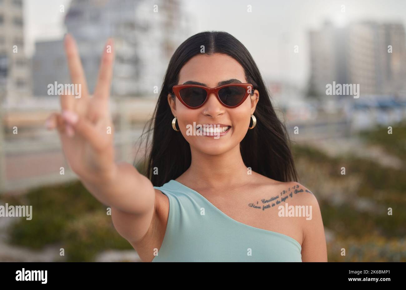 Keine Sorge, keine Zweifel. Eine schöne junge Frau, die das Friedenszeichen am Strand zeigt. Stockfoto