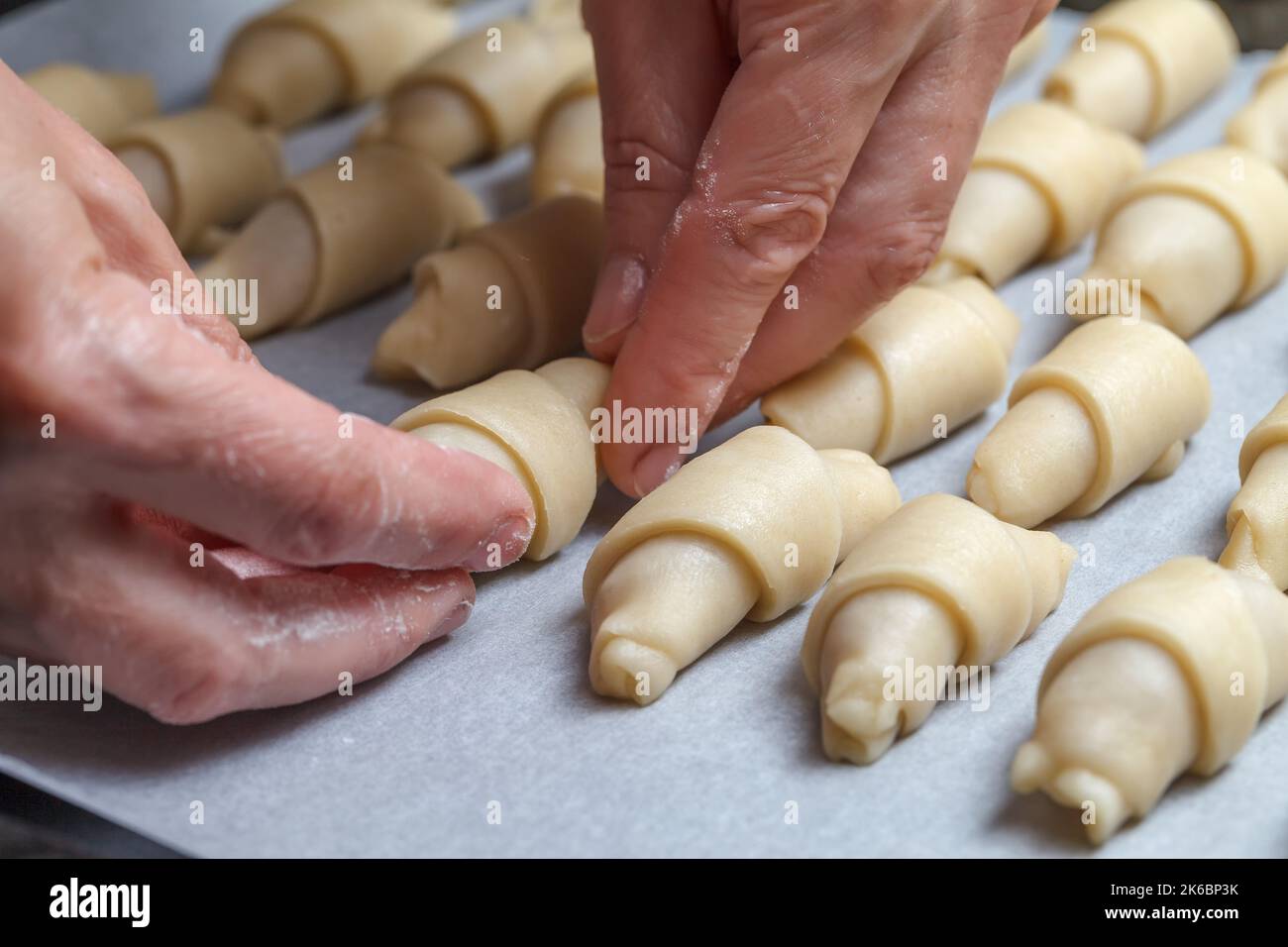 Die Hände des Konditors Rollen den Teig mit Füllung zu einer Rolle für das weitere Backen von Croissants. Französische Mini-Croissants mit fruchtiger Marmelade. Nahaufnahme. Hausgemachtes Backkonzept Stockfoto