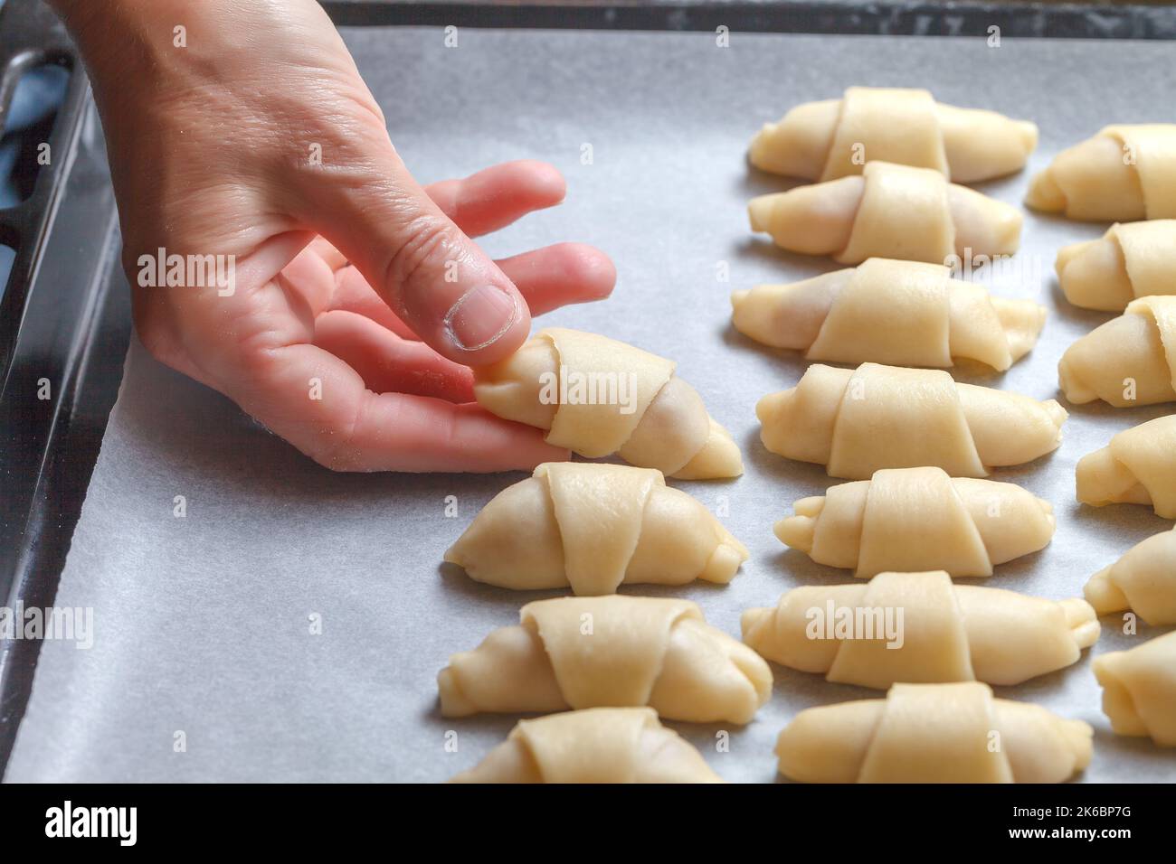 Die Hände des Konditors Rollen den Teig mit Füllung zu einer Rolle für das weitere Backen von Croissants. Französische Mini-Croissants mit fruchtiger Marmelade. Nahaufnahme. Hausgemachtes Backkonzept Stockfoto