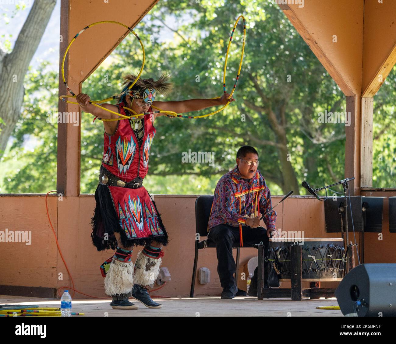 Navajo Native American Hoop Dancer in Regalia, die auf einem Festival in Moab, Utah, auftreten. Dahinter ç ein Schlagzeuger des Sängers. Stockfoto