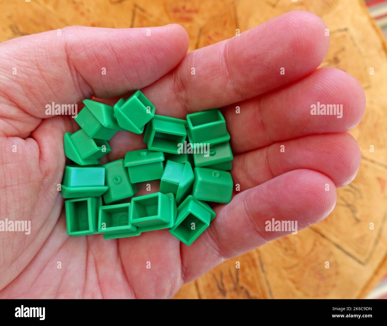 Eine Erwachsene Hand, die grüne Monopoly-Häuser zur Miete oder von hält, die Immobilien- und Wohnungsfragen des Vereinigten Königreichs vertritt Stockfoto