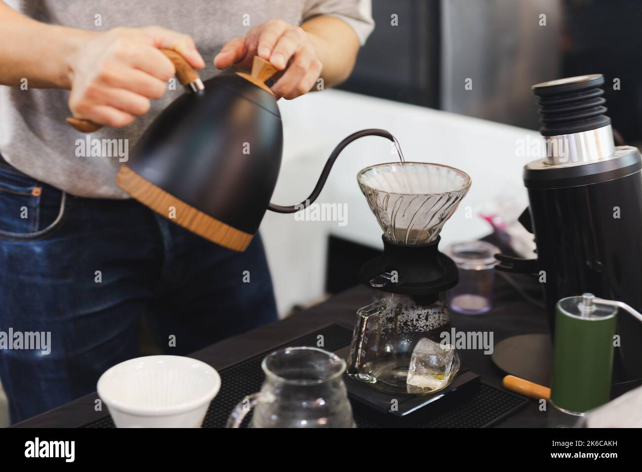 Barista gieße heißes Wasser über den Tropffilter auf den Kaffee mit rauen braunen Blasen. Stockfoto
