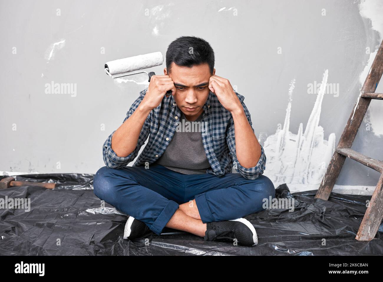 Ein junger asiatischer Mann sitzt mit Kopf in den Händen überwältigt von Heimwerkerprojekt Stockfoto
