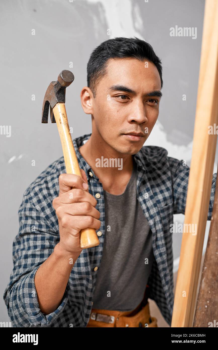 Ein seriöser asiatischer Mann verwendet Hammer, um Holz zu schlagen, während er Heimrenovierung DIY macht Stockfoto