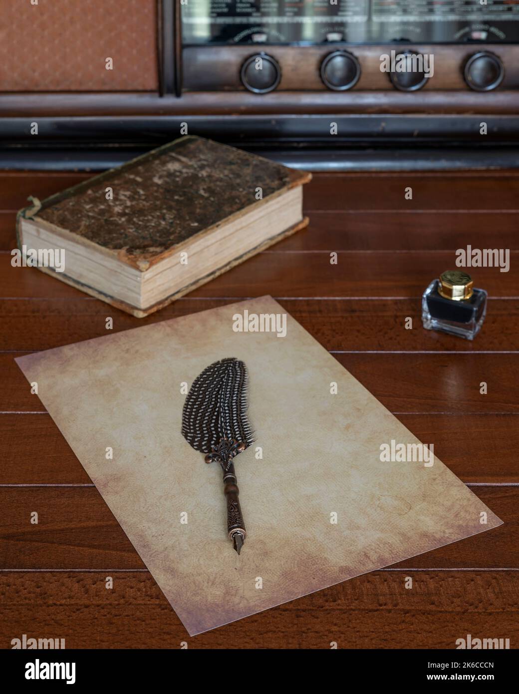 Ein Blatt antiquiertes Papier mit einem Füllfederhalter mit einer Feder darauf, auf einem Holztisch mit einer Flasche Tinte daneben und einem alten Radio und einem alten Stockfoto