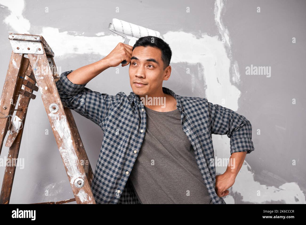 Ein attraktiver asiatischer Mann ist überwältigt, bevor er zu Hause DIY Malerei Wand beginnt Stockfoto
