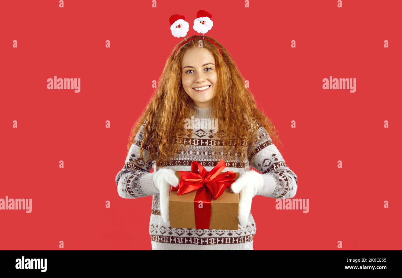 Glückliche schöne Frau isoliert auf rotem Hintergrund lächelt und gibt Ihnen Weihnachtsgeschenk Stockfoto