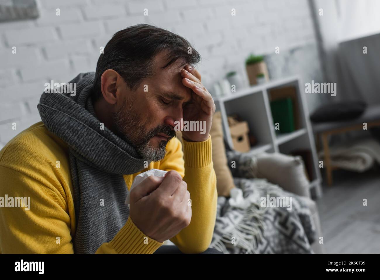 Kranker Mann in warmem Schal mit Papierserviette und leidet unter Kopfschmerzen, Stockbild Stockfoto