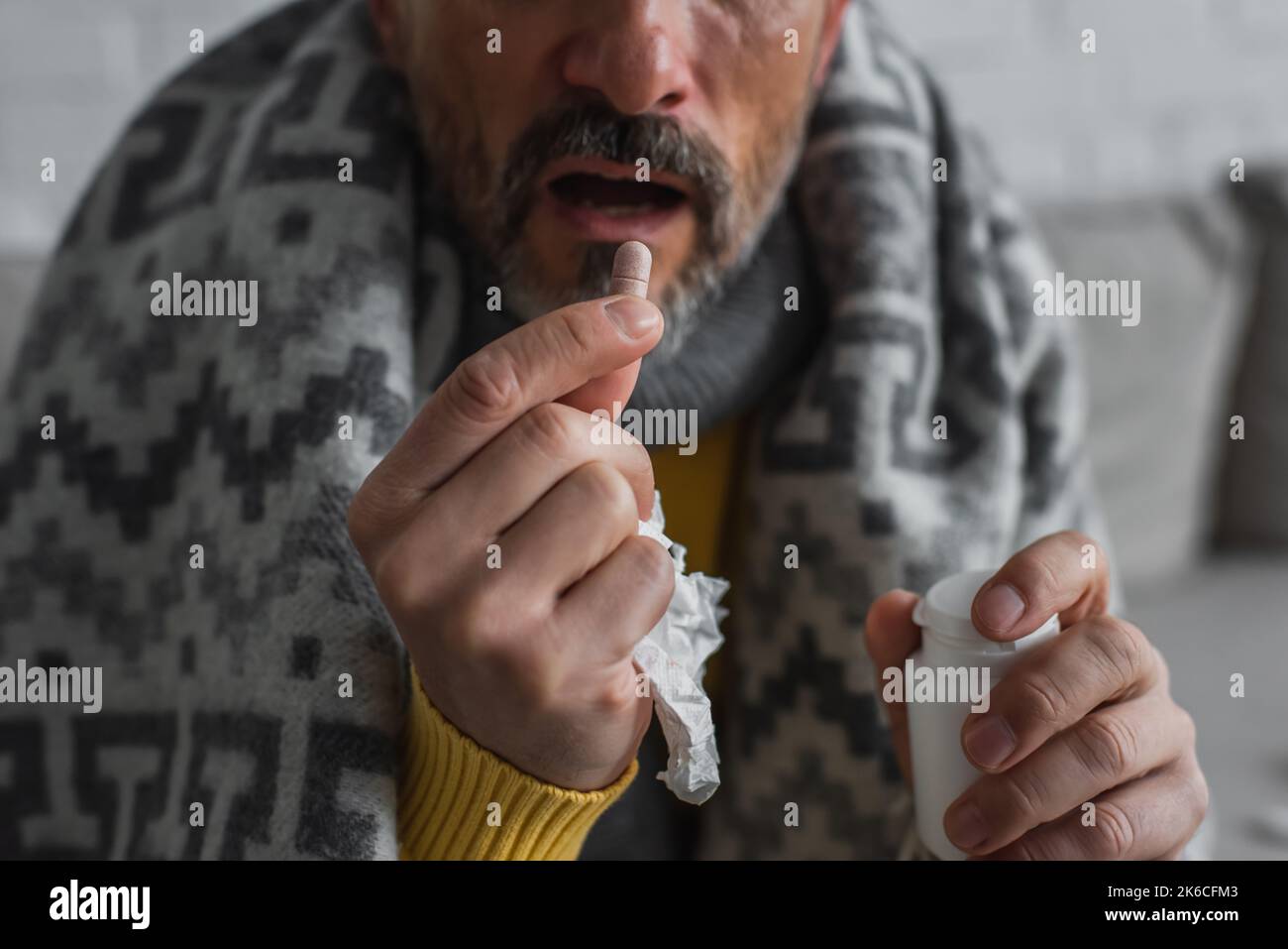 Teilansicht des erkrankten Mannes mit Papierserviette, die Pille auf verschwommenem Hintergrund nahm, Stockbild Stockfoto