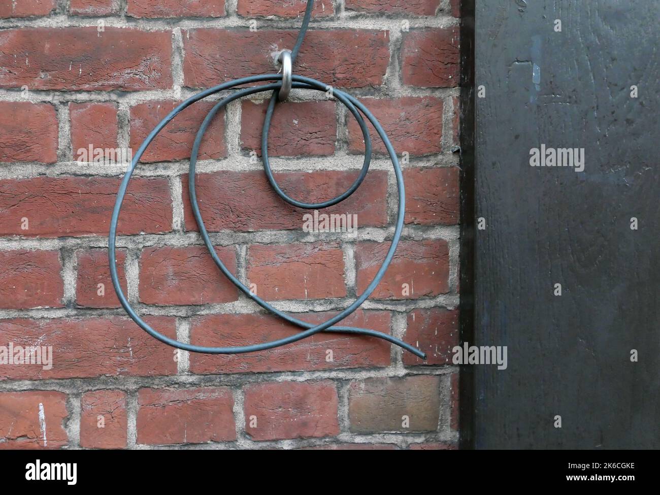 Lockerer Elektrodraht, der an der Schlaufe in der alten Ziegelwand hängt Stockfoto