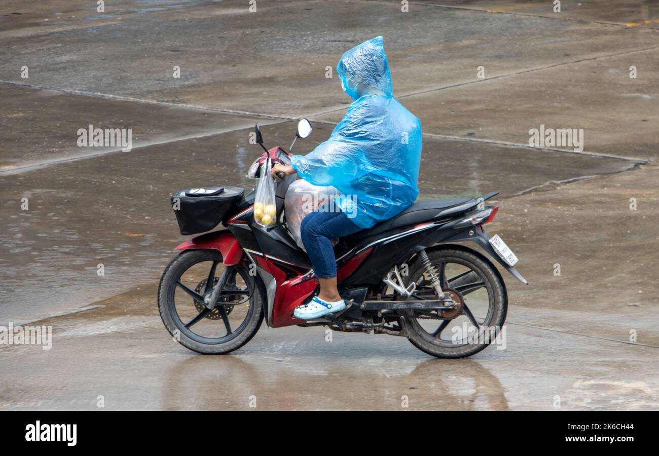 Ein Motorradfahrer im Regenmantel fährt im Regen auf einer Stadtstraße in Thailand Stockfoto