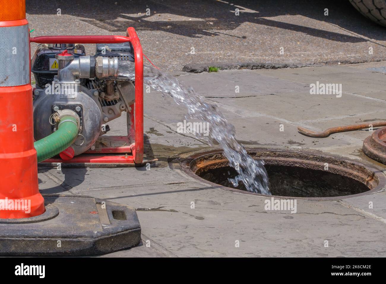 Wasserstrom, der in das Mannloch auf der Stadtstraße gepumpt wird Stockfoto