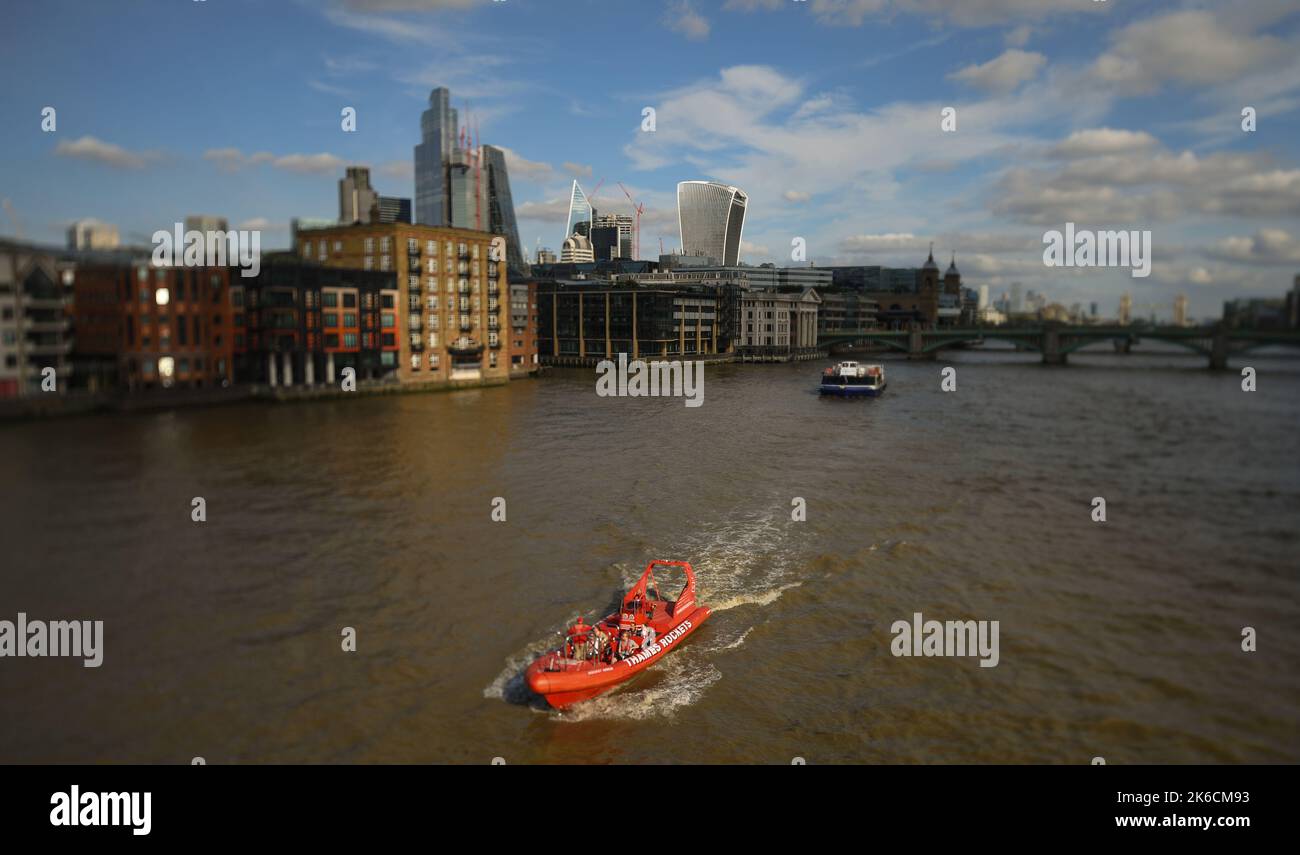 Ein Raketenboot der Themse fährt in Richtung Millennium Bridge, gefolgt von einem City Cruises Boot & Financial District im Hintergrund. Aufgenommen auf einer Shift Lens. Stockfoto