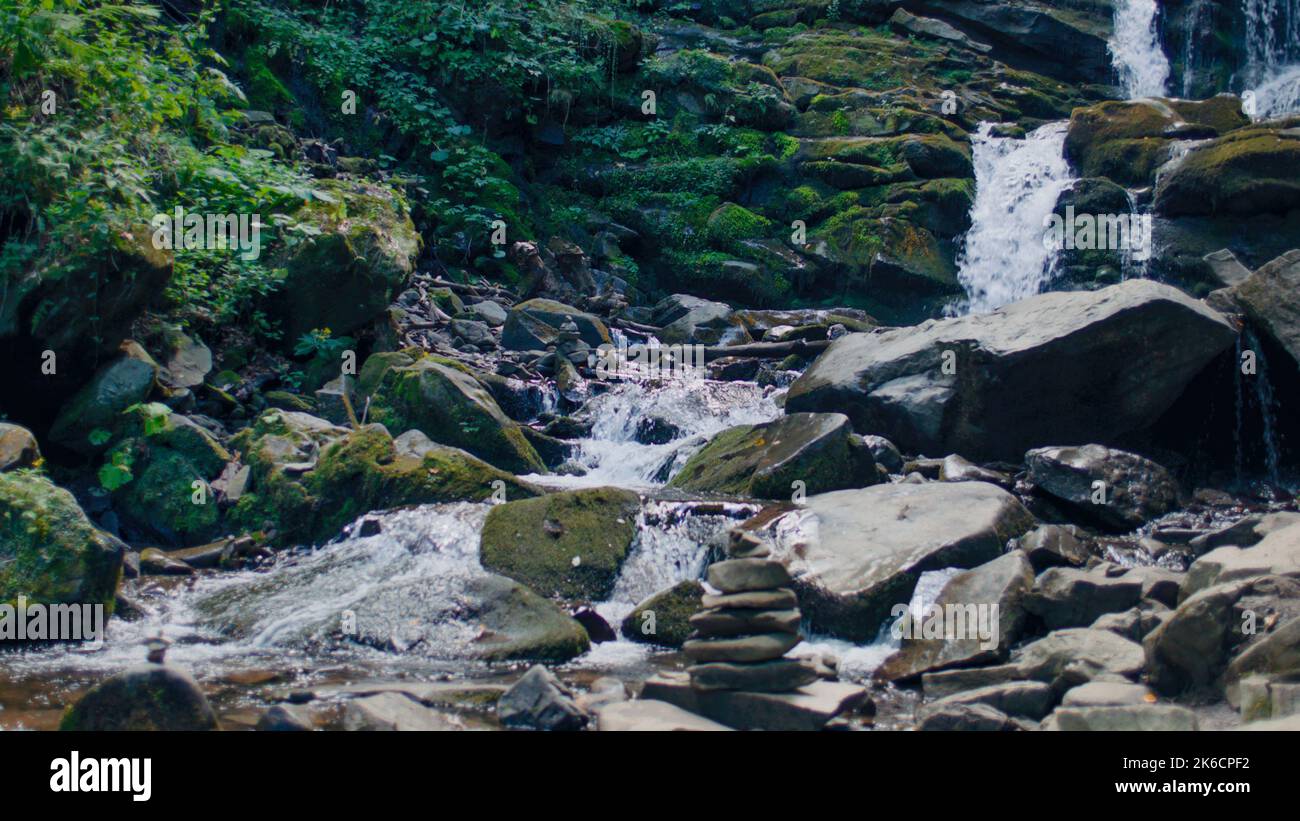 Wasserfall, der die moosigen Steine des Berges wäscht, Spritzer auf die Pflanzen fallen. Gefallene Blätter Rollen den Hügel hinunter, klarer Wasserstrom fließt zwischen den Bergen. Erstaunlich schön der Natur Stockfoto