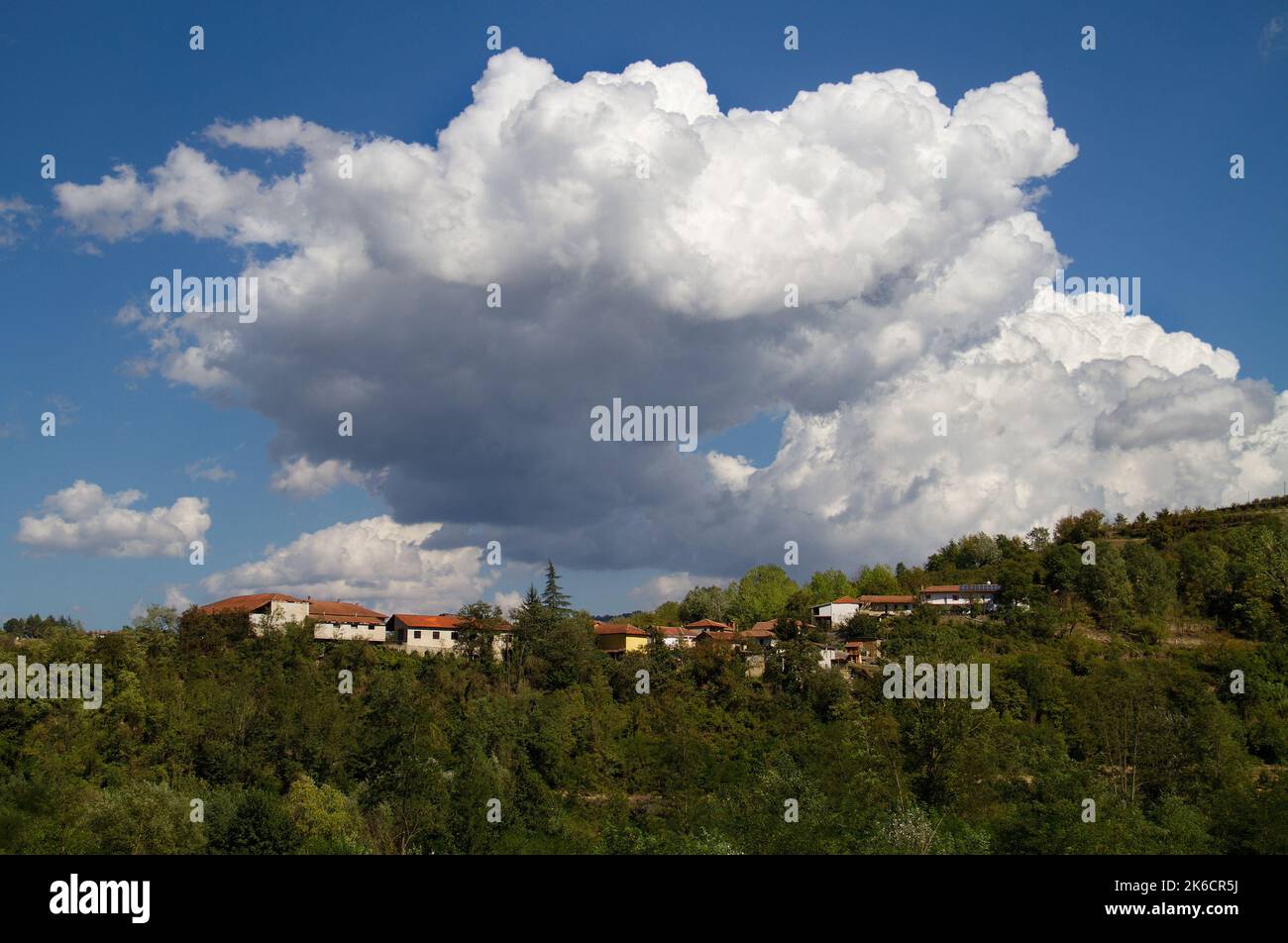 Cumulus Wolken, große weiße Wolken, über einem Dorf auf einem bewaldeten Hügel in der Toskana, Italien Stockfoto