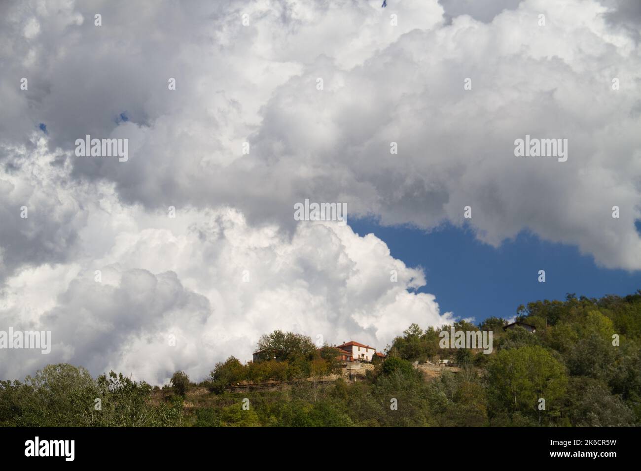 Cumulus Wolken, große weiße Wolken, über einem Dorf auf einem bewaldeten Hügel in der Toskana, Italien Stockfoto