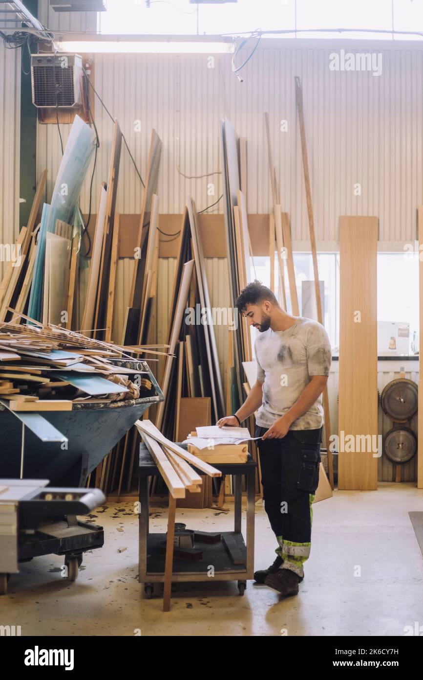 Die ganze Länge des männlichen Zimmermanns liest die Blaupause auf der Werkbank in der Werkstatt Stockfoto