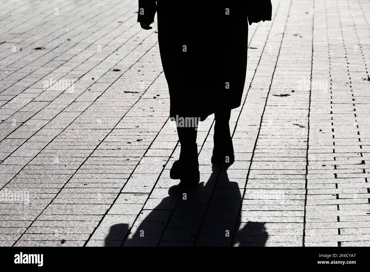 Silhouette einer einsamen Frau in Herbstkleidung, die die Straße entlang läuft, schwarzer Schatten auf dem Bürgersteig. Konzept der Einsamkeit, dramatisches menschliches Leben Stockfoto