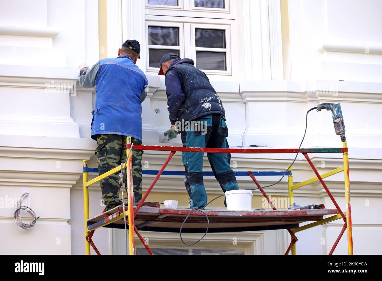 Arbeiter reparieren die Gebäudewand, die auf einer Hebebühne steht. Zwei Bauherren lackieren die Hausfassade, Bau- und Reparaturarbeiten Stockfoto