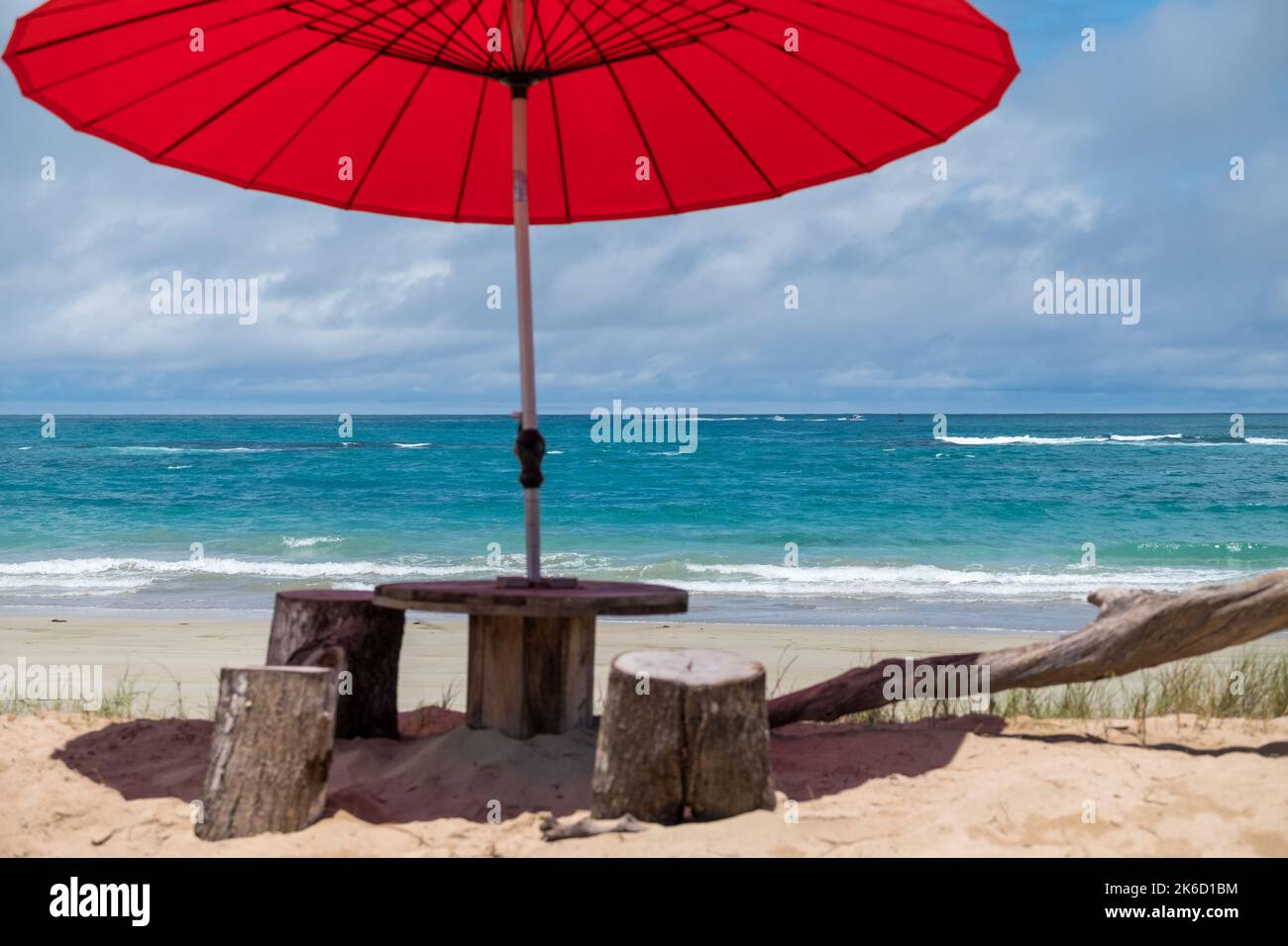 Schöner Strand mit türkisfarbenem Meer, mit einem roten Sonnenschirm und einer Bank im Vordergrund. Idilische Landschaft für den perfekten Urlaub. Stockfoto