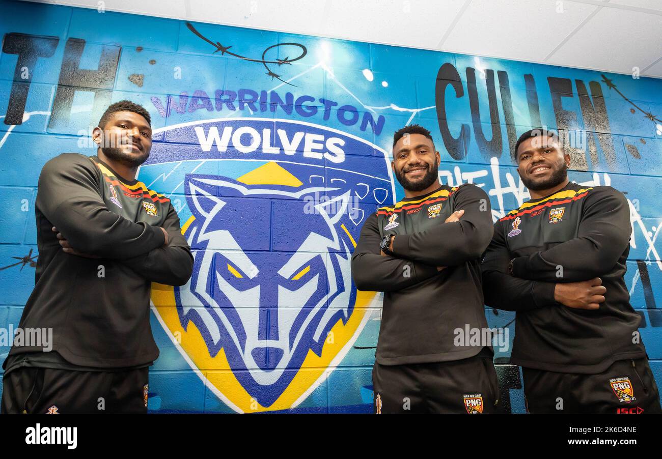 Drei Mitglieder des Papua-Neuguinea-Teams posieren vor der Warrington-Wolves-Wandkunst im Halliwell-Jones-Stadion Stockfoto