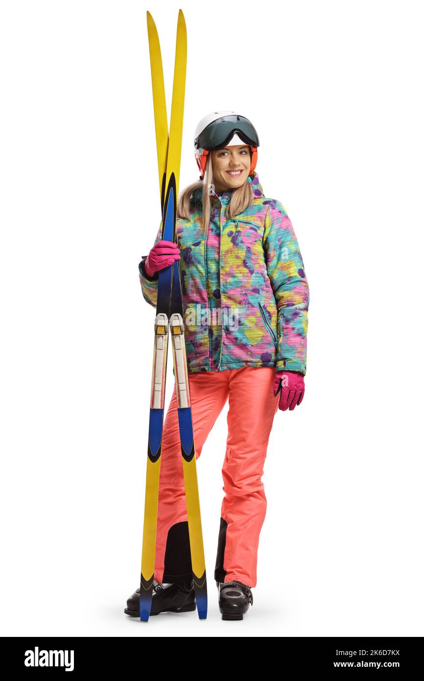 Ganzkörperporträt einer jungen Frau mit einem Helm, der steht und ein Paar Ski auf weißem Hintergrund hält Stockfoto