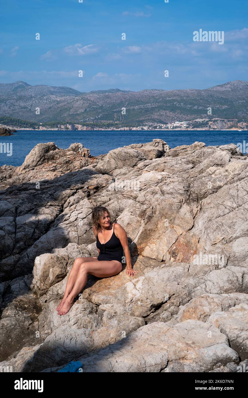 Reife Frau in einem Badekostüm, die die Sonne an einem felsigen Ufer am Meer in Kroatien genießt Stockfoto